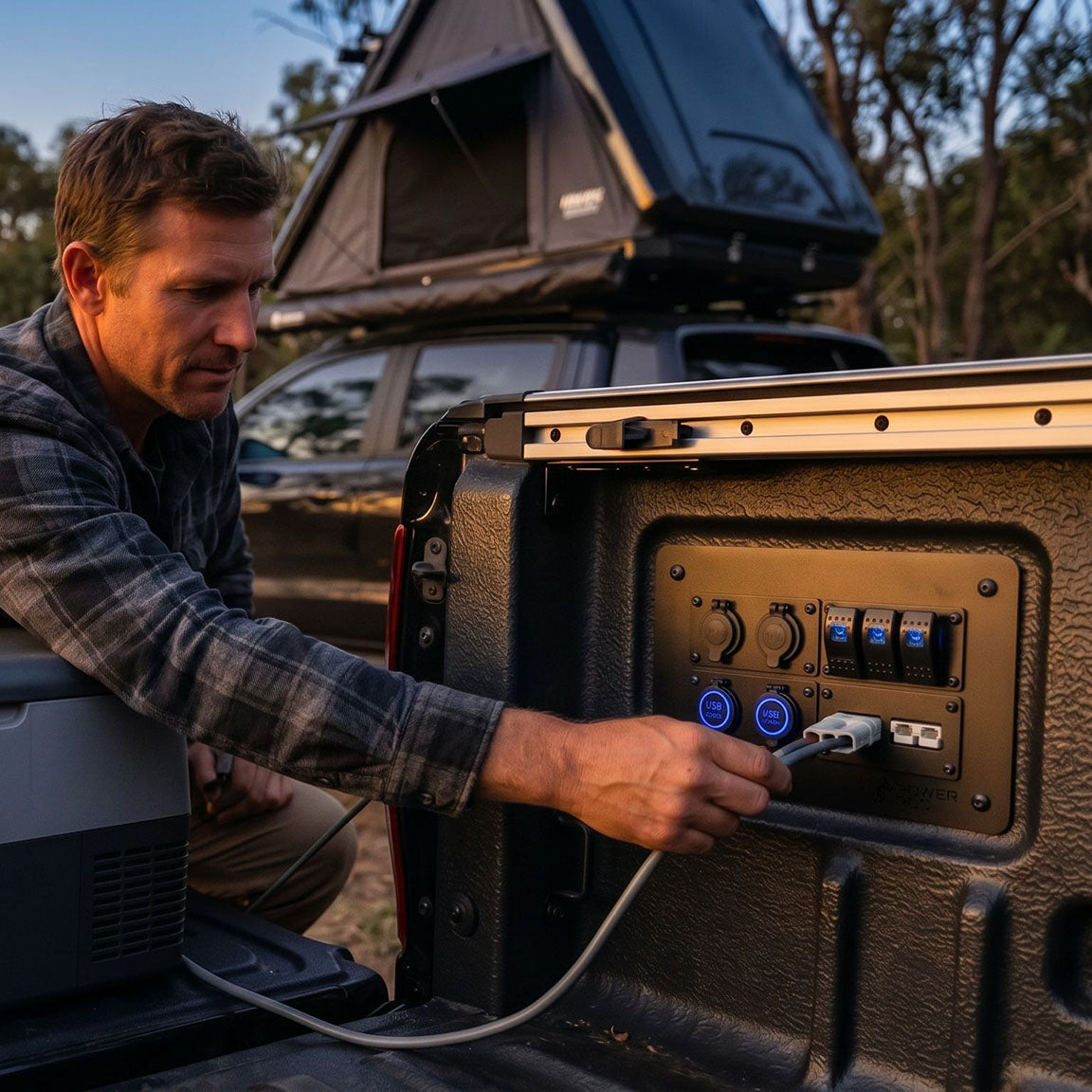 Man plugging a portable fridge into a PowerRoo Ford Ranger 12V power panel while camping